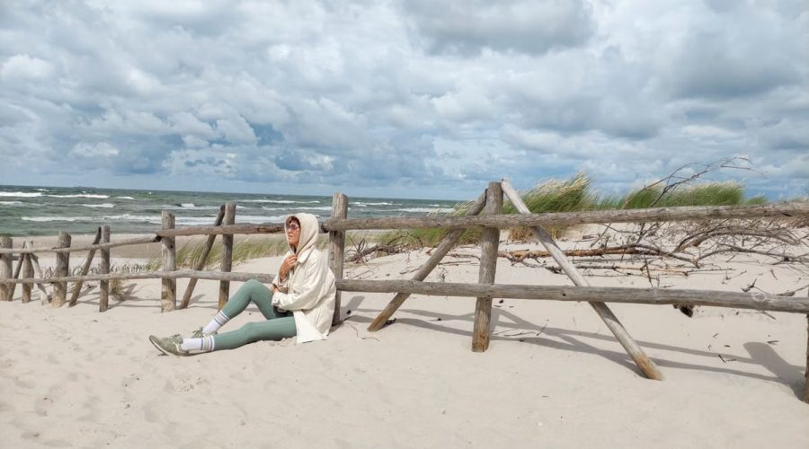 Person in casual attire sits on Baltic beach, enjoying the serene sea view.