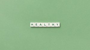 Scrabble tiles spelling the word 'healthy' on a light green background, top view.