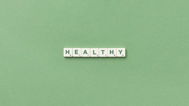 Scrabble tiles spelling the word 'healthy' on a light green background, top view.